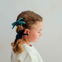 Copil purtând un set de 4 scrunchie-uri Blackberry cu fundă, vedere din profil, pe fundal gri deschis