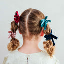 Copil purtând un set de 4 scrunchie-uri Blackberry cu fundă, vedere din spate, pe fundal roz