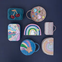 Geantă curcubeu Dreamwish, roz pastel alături de alte accesorii Mimi & Lula, pe fundal bleumarin